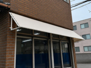 ビルの出入り口に設置されたアイボリーの庇テント